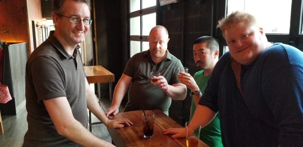Four people with drinks standing around a table in a bar.