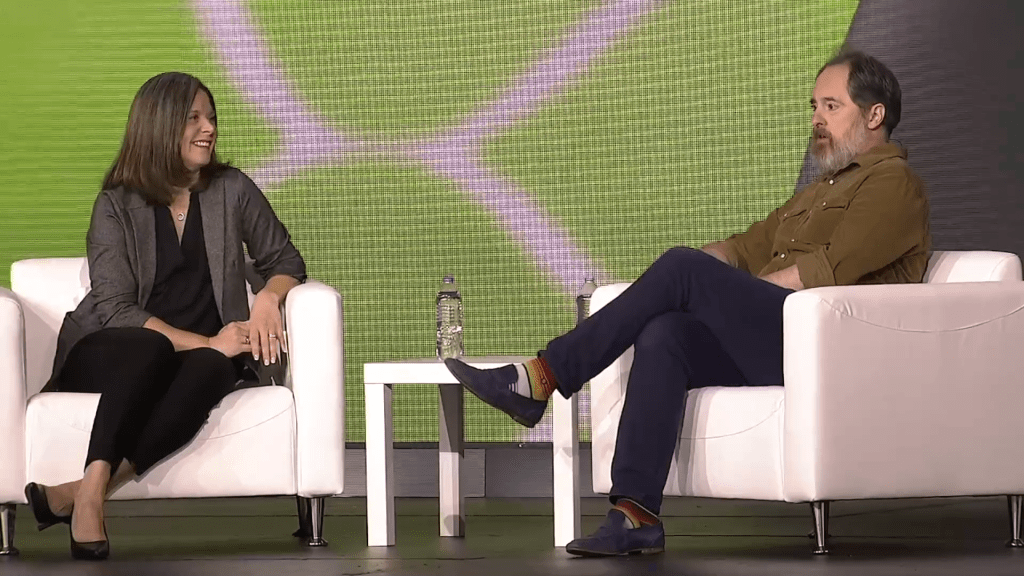 Two people sitting on white chairs on a stage (Hannah Grap, Sitecore and Brendan Hunt, actor) at Sitecore Symposium 2024 in Nashville