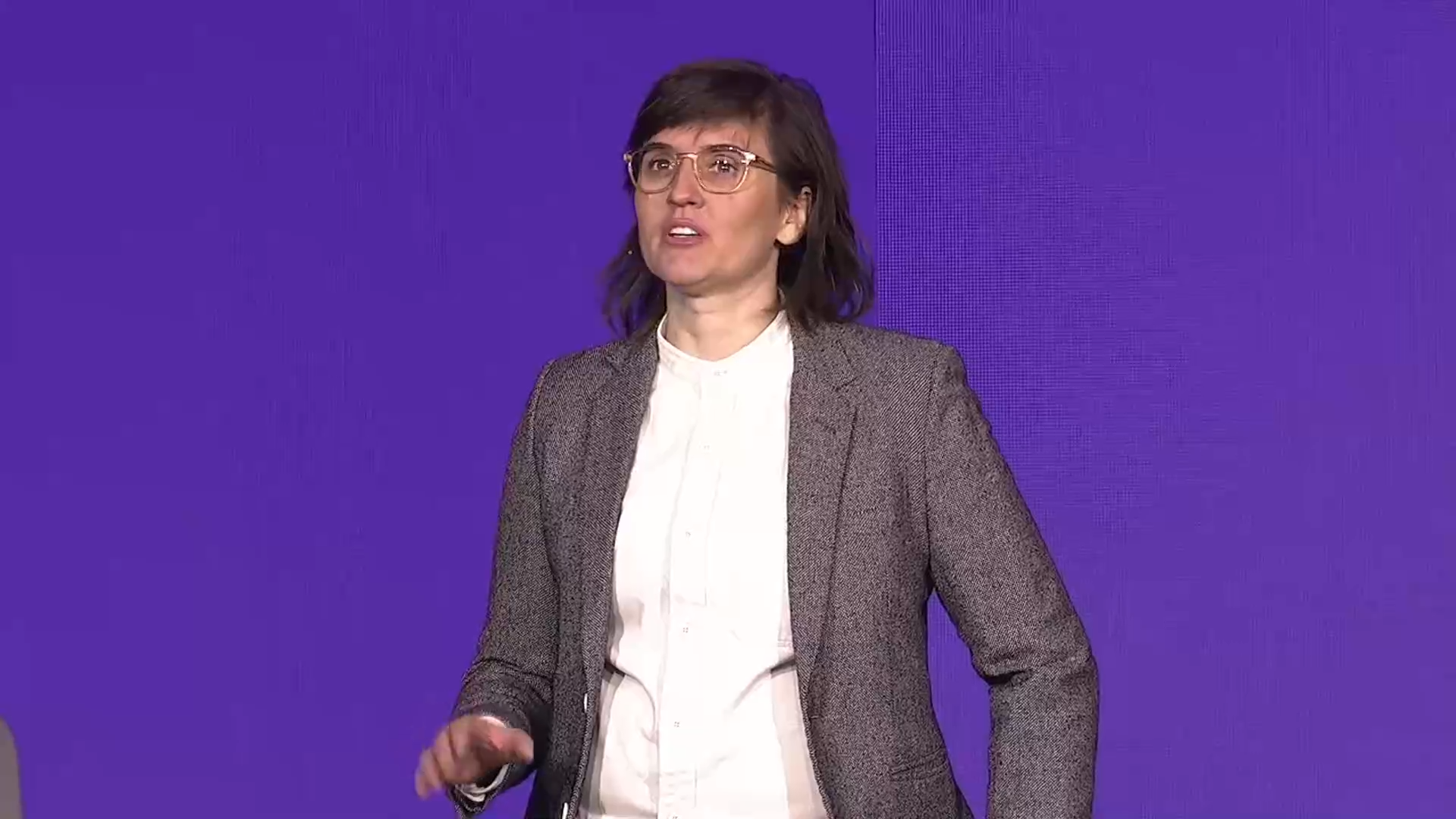 Person in whiTe shirt and grey suit jacket (Liz Nelson) on stage at Sitecore Symposium 2024